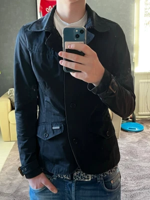 Fieldjacket från Woolrich - Säljer en jacka från Woolrich med klassisk krage, knappar och dragkedja framtill. Jackan har justerbara spännen vid ärmsluten och två fickor med knappar. Storlek S/Xs.  Modellen är 176 cm och väger 61 kg. Passar folk mellan typ 165-178 cm. Hör av er om ni har några frågor!🤗