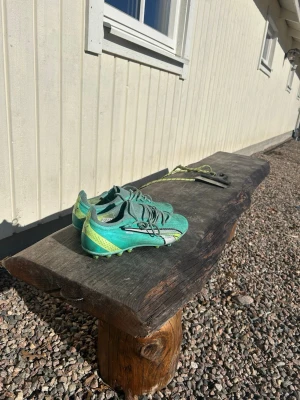 Gröna Puma fotbollsskor med dobbar - Snygga gröna fotbollsskor från Puma med silverfärgade och svarta detaljer samt gula inslag vid hälen. Skorna har klassisk snörning och är designade med dobbar för spel på gräs. Perfekta för dig som vill sticka ut på planen. Köpte skorna för ett år sen och har kanske använts som Max i 3 månader. Köpte skorna för 1 400 kr. 