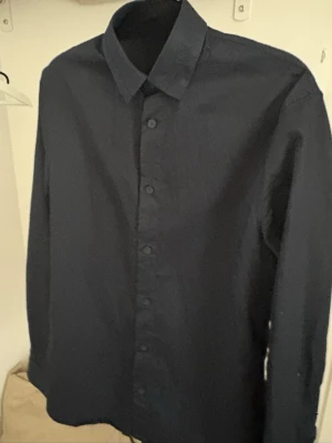 Mörkblå skjorta från Armani Exchange - Stilren mörkblå skjorta från Armani Exchange med klassisk krage och knäppning framtill. Skjortan har lång ärm och är tillverkad i ett lätt och bekvämt material som passar perfekt till en snygg och enkel look.