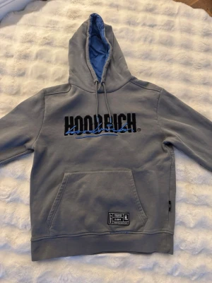 Grå Hoodrich set - Snygg grå Hoodrich set  med svart och blått tryck på bröstet. Stor känguruficka framtill och patch nertill. Huvan har blått innerfoder och dragsko. Perfekt för en streetwear-look.