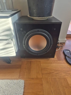 Dynavoice Definition SW10 subwoofer - Kraftfull svart trådlös subwoofer från Dynavoice, modell Definition SW10. Snygg och robust design med rund högtalarelement på framsidan och flera anslutningsmöjligheter på baksidan. Perfekt för att boosta basen i hemmabiosystemet.