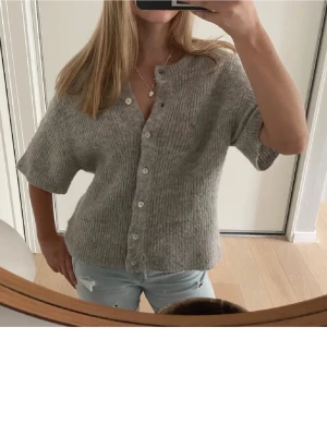 Grå ribbstickad kofta med kort ärm - Mysig grå ribbstickad kofta med korta ärmar och knappar framtill. Köpte förra året och har använts en del men i bra skick. Skriv för fler bilder!💞