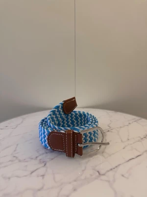 Ljusblå vitt flätat bälte - Tja säljer helt nya svenska klassiska flätade bälten från Bältgallerian i storlek 105cm lång och 3,5cm bred. Dem är i ett elastiskt material och finns i flera olika färger i min profil