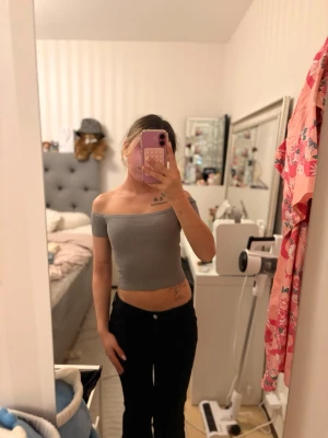 Grå offshoulder croppad topp - Snygg grå croppad topp med offshoulder-design och korta ärmar. Perfekt för dig som vill ha en trendig och enkel stil. Toppens passform är tight och den är tillverkad i ett mjukt material som sitter skönt mot kroppen.