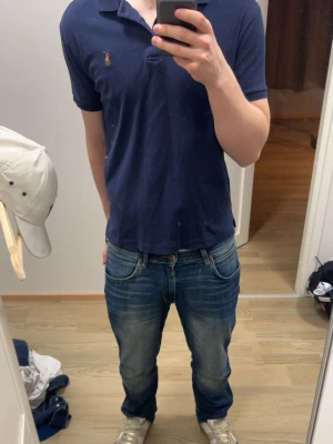  pikétröja Ralph Lauren - Mörkblå pikétröja från Polo Ralph Lauren med korta ärmar och krage. Tröjan har knappar vid halsen och den ikoniska broderade loggan på bröstet.