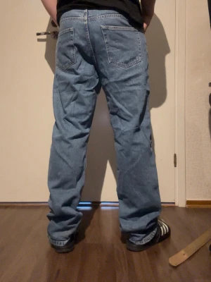 Baggy ljusblå jeans i klassisk modell - Baggy ljusblå jeans med raka ben och fem fickor. Jeansen har en klassisk passform med hög midja och bred siluett, perfekta för en avslappnad streetstil. Tillverkade i denim med tydliga sömmar och traditionell design.
