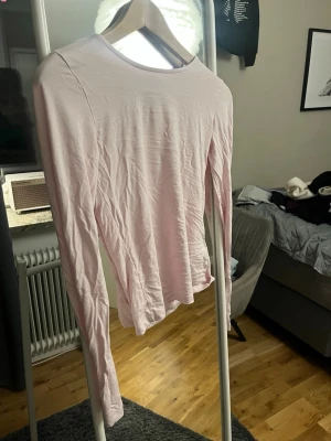 Ljusrosa långärmad topp - En enkel och stilren ljusrosa långärmad topp med rund halsringning. Toppen är figurnära och passar perfekt till jeans eller kjol. Tillverkad i mjukt material som känns skönt mot huden.