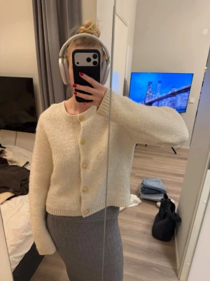 Krämvit kofta med träknappar - Mysig krämvit kofta med rund halsringning och stora träfärgade knappar. Koftan är stickad i ett fluffigt material och har en rak, något boxig passform med långa ärmar och ribbade muddar. Perfekt för lager-på-lager och chill vibes.