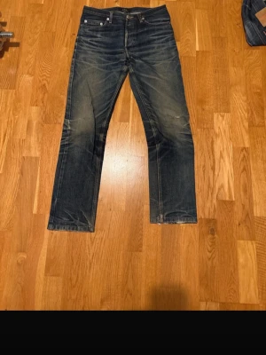 A.P.C. New Cure jeans mörkblå - Säljer ett par mörkblå jeans från A.P.C. i modellen New Cure. Jeansen har klassisk femficksdesign, raka ben och snygga slitningar vid knäna. Tillverkade i kraftig denim med orangea sömmar och metallknappar. Perfekta för en stilren och avslappnad look.