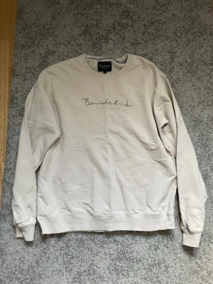 Beige sweatshirt från Bondelid - Beige sweatshirt från Bondelid med rund halsringning och tryckt logga på bröstet. Tröjan har långa ärmar, ribbade muddar och är tillverkad i mjukt material som passar perfekt till en avslappnad stil.