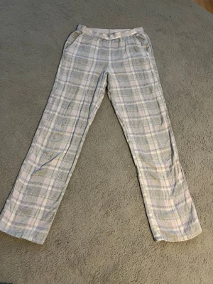 Rutiga pyjamasbyxor i pastellfärger - Mysiga pyjamasbyxor med rutigt mönster i ljusgrått, vitt och ljuslila. Byxorna har rak passform och resår i midjan för extra komfort. Material: 100% Bomull.