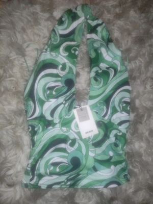 Grön mönstrad halterneck topp Bik Bok - Snygg halterneck topp från Bik Bok med grönt, vitt och svart psykedeliskt mönster. Djup urringning framtill . Stretchigt material som sitter tajt och bekvämt. Perfekt för att sticka ut med en färgglad look.