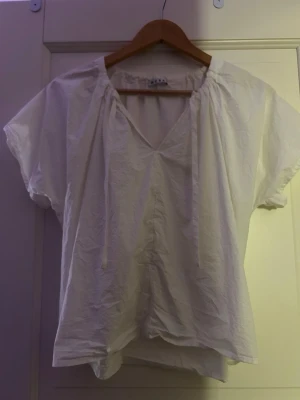 Vit blus med knytband i halsen - Vit blus med v-ringning och knytband från Wera. Använd fåtal gånger. 