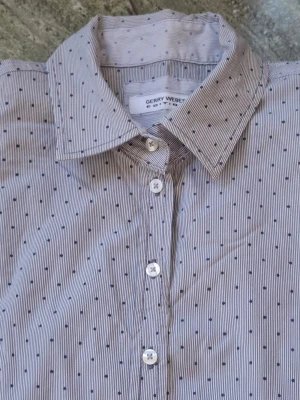 Randig skjorta från Gerry Weber - Klassisk skjorta från Gerry Weber med tunna blå ränder och små svarta detaljer. Skjortan har lång ärm, krage och knäppning framtill. Perfekt till jeans eller kostymbyxor. Bystmått: från armhåla till armhåla 50 cm  Studsmått: från sida till sida längst ner 55 cm Längd: uppifrån och ner 60 cm