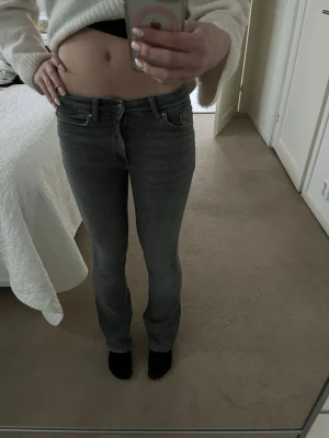 Grå raka jeans med låg midja - Säljer ett par grå jeans med låg midja och raka ben. Klassisk femficksmodell med dragkedja och knapp framtill. Jeansen har en snygg tvättad look och passar perfekt till en avslappnad stil. Materialet känns som bomullsdenim.