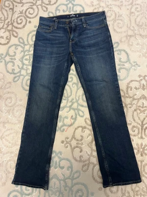 Mörkblå bootcut jeans hollister - Säljer ett par mörkblå bootcut jeans med klassisk femficksdesign och snygga slitningar framtill. Jeansen har normal midja och raka ben. Perfekta till en avslappnad stil och passar till det mesta i garderoben. Storlek 32 30