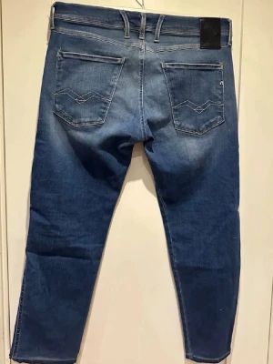 Replay Anbass - Säljer ett par blå jeans från Replay med raka ben och klassisk femficksmodell. Jeansen har snygga slitningar framtill och kontrastsömmar på bakfickorna. Materialet är mjukt denim med lite stretch för extra komfort. Perfekta till en avslappnad stil.