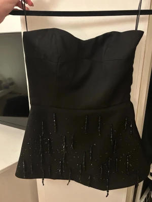 Fest topp H&M - Snygg svart tubtopp från H&M. Toppen har dekorativa pärlor och paljetter på nederdelen som ger extra edge. Perfekt för dig som vill sticka ut med en elegant men cool look.