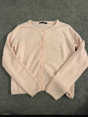 Ljusrosa kofta från 157 - Söt ljusrosa kofta från 157 med rund halsringning och knäppning framtill. Koftan har långa ärmar och är stickad i ett mjukt material, perfekt att slänga på sig när det är lite kyligt ute.(pris kan alltid diskuteras)💞