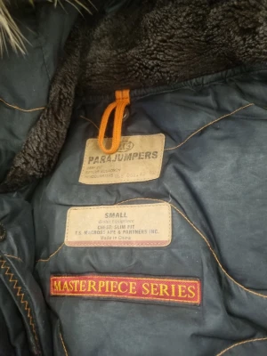 Svart vindjacka från Parajumpers - Snygg svart vindjacka från Parajumpers Masterpiece Series med gul detalj och patch på ärmen. Jackan har mjukt foder, dragkedja och flera fickor. Perfekt för dig som vill ha en stilren och funktionell jacka med coola detaljer. Väldigt varm jacka i storlek S använd. 