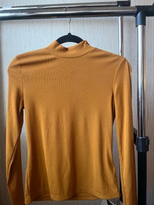 Senapsgul ribbad polotopp - Senapsgul polotopp med ribbad struktur och lång ärm. Hög hals och figurnära passform. Pris kan diskuteras!