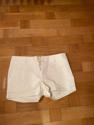 Vita lågmidjade shorts från Lacoste - Snygga vita shorts från Lacoste med två knappar och dragkedja framtill. Klassisk design med fickor både fram och bak. Perfekta för varma dagar och enkel att matcha med olika toppar ☀️
