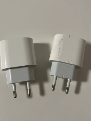 Två vita USB-laddare till mobil - Säljer två vita USB-väggadaptrar med europeisk kontakt, perfekta för att ladda mobilen eller surfplattan. Klassisk kompakt design i plast, passar de flesta USB-kablar. Smidig att ha med sig i väskan eller använda hemma.