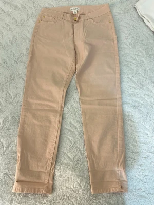 Beiga/ljusrosa jeans från Lindex - Snygga beiga/ ljusrosa jeans från Lindex med rak passform och klassiska fem fickor. Jeansen har bälteshällor och gylf med dragkedja och knapp. 