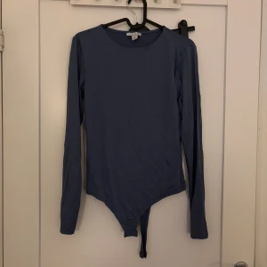 Blå långärmad body - Säljer en stilren blå body med långa ärmar och rund halsringning. Perfekt att styla med jeans eller kjol. Mjukt och stretchigt material för en bekväm passform.