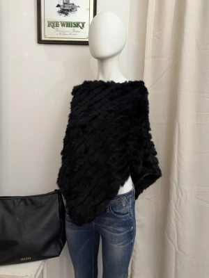 Soyaconcept svart kaninpäls poncho  - Säljer en svart poncho i mjuk kaninpäls med diagonal struktur. Ponchon har en lös passform och ger en lyxig känsla, perfekt att slänga över en outfit för extra värme och stil. Inga synliga knappar eller dragkedjor, enkel att dra över huvudet. Ny med prislapp. 