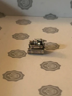 Pandora berlock studentmössa 2021 - Söt berlock från Pandora i silverfärgad metall, formad som en stapel böcker med en studentmössa och årtalet 2021 ingraverat. Perfekt detalj till armband för att minnas examen eller studenten.