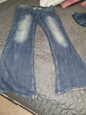 Blå bootcut jeans med slitningar - Säljer ett par blå bootcut jeans med snygga slitningar och ljusa partier framtill. Jeansen har klassisk femficksmodell och normal midja. Perfekta för dig som gillar en avslappnad och trendig look. Materialet är denim. Storlek 33/32 använd fåtal gånger 