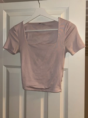 Ljusrosa croppad topp med fyrkantig ringning - En fin ljusrosa croppad topp med korta ärmar och fyrkantig ringning. Tillverkad i mjukt och stretchigt material som sitter superfint. 