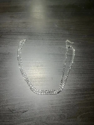Silverfärgat kedjehalsband - Snyggt halsband i silverfärg med dubbla kedjor. Kedjan har en klassisk, lite bredare länkdesign som ger ett stilrent och trendigt intryck. Perfekt för dig som gillar minimalistiska accessoarer med lite edge. Inget synligt märke på halsbandet.