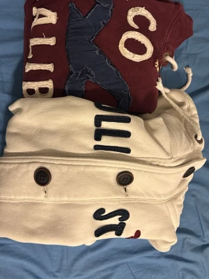 bundle vara - privat kund - ( HÖGER) Väldigt sällsynt och vintage Hollister hoodie med knappar | Tröjan är i väldigt bra skick utan defekter, handledarna kan uppfattas vara lite större| Längd ≈ 63cm, Bredd armhåla-amrhåla ≈ 53cm | Modell 175cm, 68kg | Hör av vid ytterligare frågor och priset kan diskuteras vid snabbt köp! | (VÄNSTER VINRÖD) Extremt sällsynt och unik Hollister Hoodie med tryck | Hoodien har en unik sliten & distressed design! | Mycket bra skick | Storlek S | Längd≈ 65 cm, Bredd 54 cm under armhål-armhåla| 