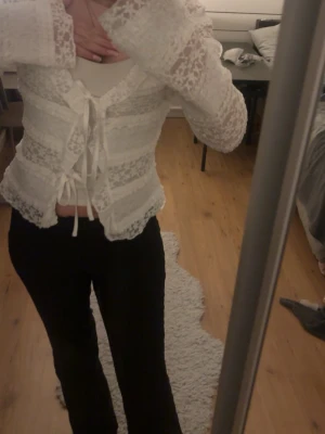 Vit spetsblus med snörning - Supersöt vit blus i spets med långa ärmar och snörning framtill. Blusen har en croppad passform och romantiska detaljer som ger en trendig look. Perfekt att styla med jeans eller kjol för en cool vibe.