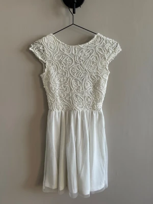 Bubbleroom Vit kort klänning med spetsdetaljer - Superfin vit kortklänning med broderad spets upptill och lätt, flowy kjol i tunt tyg. Klänningen har rund halsringning och korta ärmar. Perfekt för dig som gillar romantiska detaljer och en feminin look.