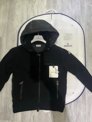 Moncler cardigan  - Hej! Jag säljer nu en limited edition Moncler cardigan med en luva. Den är i jättebra skick endast andvänd 2/3 gånger och den har inte några defekter eller liknande. Den är äkta och köpt ifrån NK stockholm för inte så sedan och kvittot finns. Allt i bilderna ingår med jackan som moncler dustbag lapprna osv. Hör av er vid minsta lilla fråga! 👍