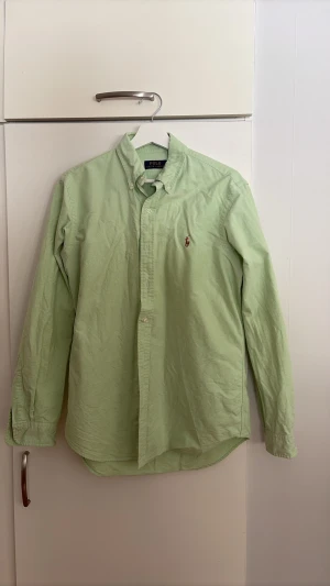Ljusgrön skjorta från Polo Ralph Lauren - Klassisk ljusgrön skjorta från Polo Ralph sopar stilen med button-down krage och broderad logga på bröstet. Skjortan är långärmad och har knappar framtill. Perfekt för dig som vill ha en clean och stilren look. Jag är 190 och den passar bra på mig.