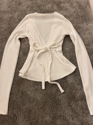 Vit topp med v-ringning - Vit långärmad topp från Nelly med knytning i ryggen🎀 Funkar både som fest topp eller att ha till vardags🥂🏫 Säljs inte längre på nellys hemsida
