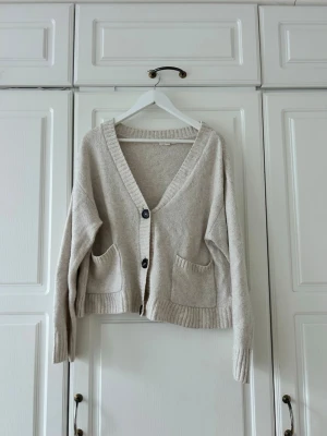 Beige kofta med fickor och knappar✨✨💖 - Mysig beige kofta med två stora framfickor och ribbade muddar. Koftan har v-ringning och stängs med två mörka knappar framtill. Perfekt oversized passform och mjukt material som känns skönt mot huden.