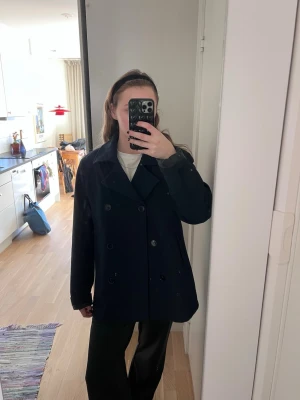 Svart skepparkavaj med dubbelknäppning - Klassisk mörkblå skepparkavaj med bred krage och dubbelknäppning framtill. Jackan har en rak passform och är tillverkad i ett kraftigt material som passar perfekt till kalla dagar. Snygg och tidlös design som funkar till många olika stilar. Storlek L, men jag är S/M och funkar fint på mig. Fint skick! 