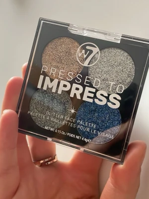 W7 Pressed to Impress Glitterpalett - Säljer en fyrfärgad glitterögonskuggspalett från W7 med nyanser i guld, silver, blått och mörkgrått. Paletten har pressade skuggor i rund form och genomskinligt lock. Perfekt för dig som älskar att experimentera med färg och glitter.