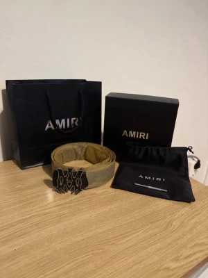 Amiri svart bälte med metallspänne - Säljer ett svart bälte från Amiri med ett stort, unikt metallspänne i silverfärg med Amiri-logga. Bältet är gjort i skinn och har en stilren, modern look. Perfekt accessoar för att lyfta din outfit.