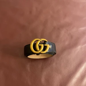 Svart Gucccii skärp med GG-spänne - Snyggt svart bälte från Guki i äkta skinn med ikoniskt GG-spänne i guld. Bältet är stilrent och har en klassisk form som passar till jeans eller kostymbyxor. Märket är stämplat på insidan och spännet är i metall med matt finish.