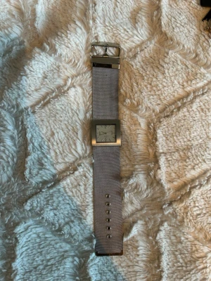 Silverfärgad fyrkantig klocka - Stilren klocka med fyrkantig urtavla i silver och matchande mesh-armband. Urtavlan har minimalistisk design med tydliga markeringar och metallspänne. Perfekt accessoar för dig som gillar enkel och modern stil. Vet inte om det är batteri eller inte i klockan 