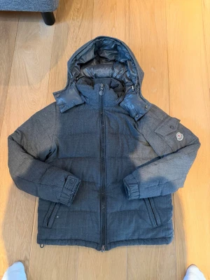 Moncler montenevro - Snygg grå dunjacka från Moncler med avtagbar huva och dragkedja framtill. Jackan har två fickor med dragkedja och Moncler-logga på ärmen. Fodrad insida och klassisk pufferstil som håller dig varm under kalla dagar. Har kvitto och priset kan gå ner vid snabb affär.