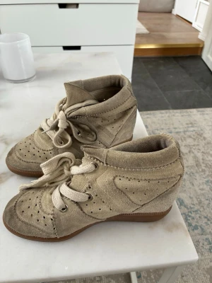 Beige höga Isabel marant sneakers i mocka - Snygga beige Isabel marant sneakers med klack. Smutsiga och slitna där fram men kan gå att tvätta bort lite. Resten är i bra skick 💕 passar mig som har 37 i skostorlek