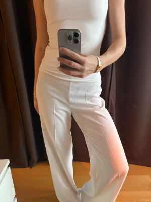 Vita vida kostymbyxor - Säljer ett par vita kostymbyxor med hög midja och vida ben. Byxorna har pressveck framtill för en clean look och är tillverkade i ett mjukt, lätt material som ger en snygg siluett. 