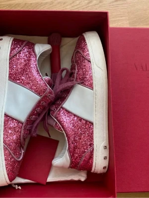Valentino rosa glitter sneakers - Snygga sneakers från Valentino med rosa glitterpaneler, vita läderdetaljer och vinröda skosnören. Skorna har en låg silhuett och coola nitar på hälen i storlek 37
